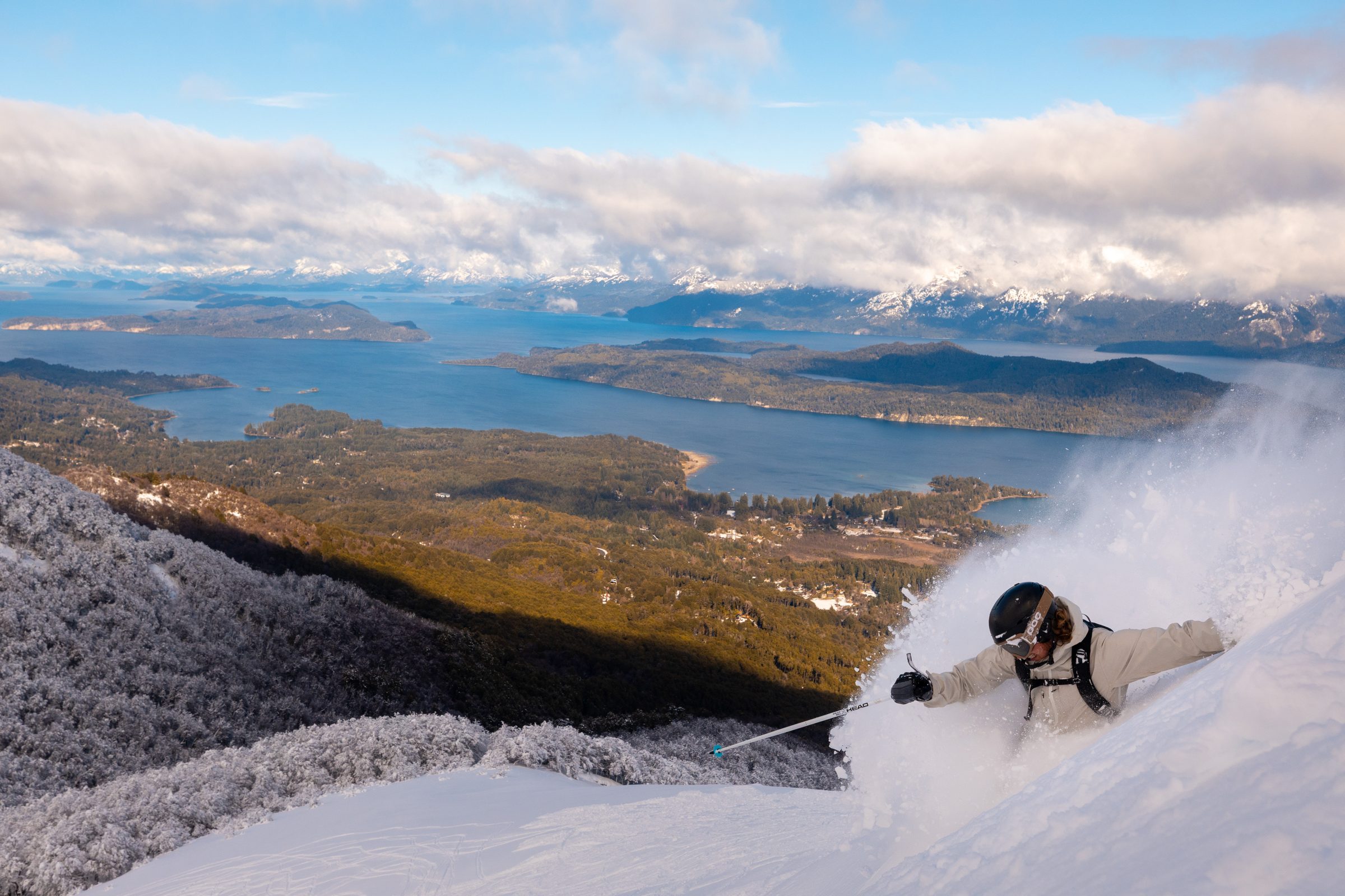 Skier descending a snowy ridge above a mountain lake and valley